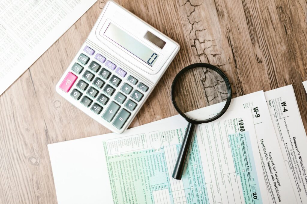 irs audit defense — tax forms laid out with a calculator and magnifying glass on a wooden surface, perfect for finance themes