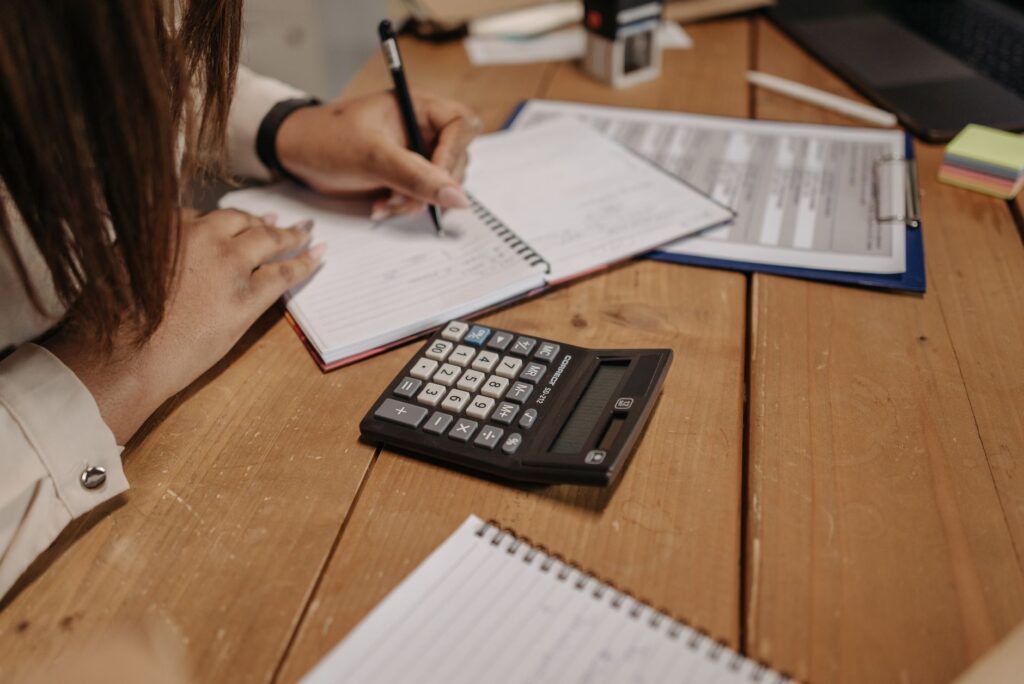 bookkeeping services small business — woman writing notes with a calculator on a wooden desk, focusing on work and accounting