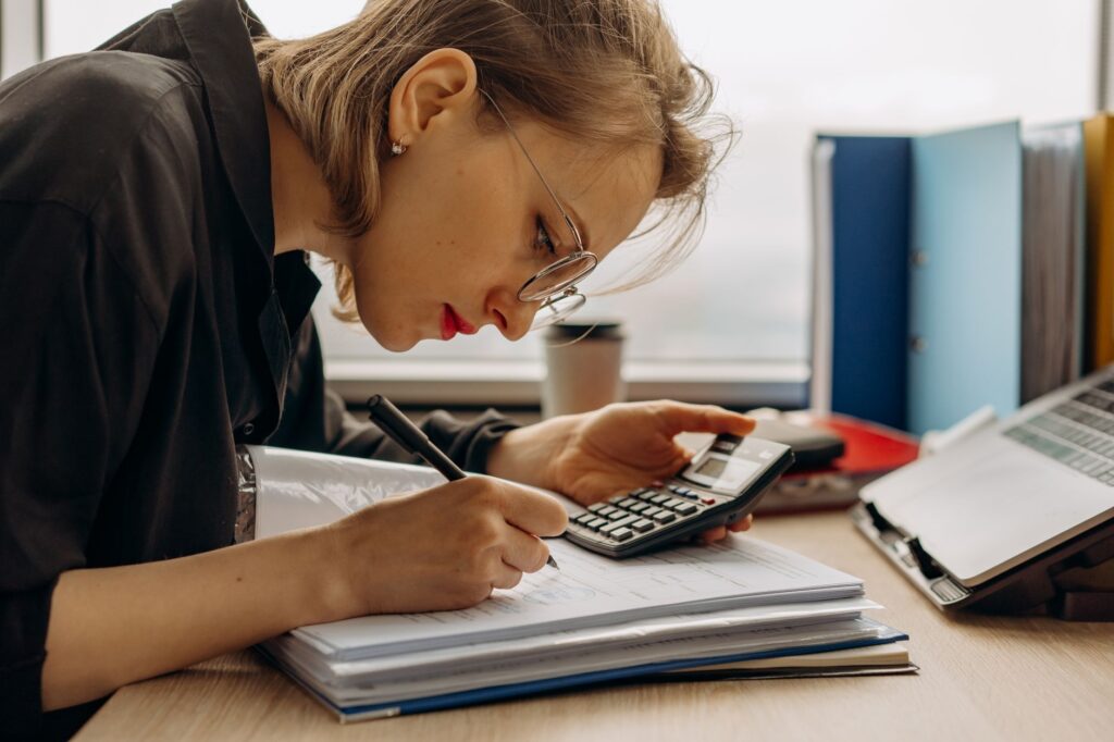 small business bookkeeping services near me — young woman diligently working on accounting with a calculator and documents. p