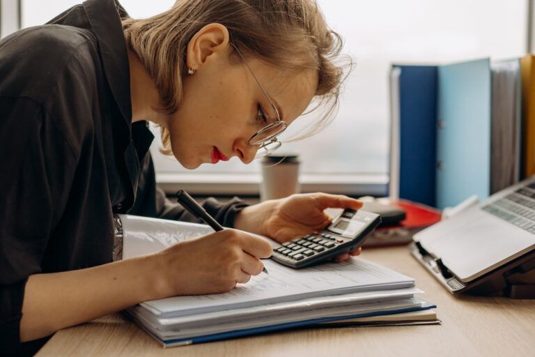 small business bookkeeping services near me — young woman diligently working on accounting with a calculator and documents. p