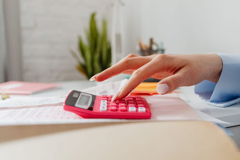 bookkeeping services small business — a close-up image of a person's hand using a red calculator on a desk with paperwork.